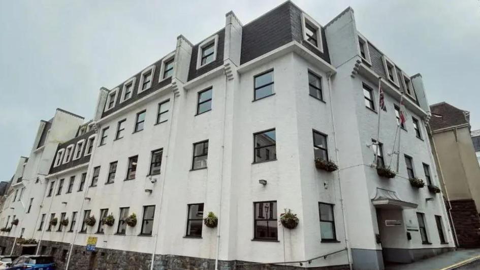 Edward T Wheadon. A white building with multiple floors. it has black windows and hanging baskets.