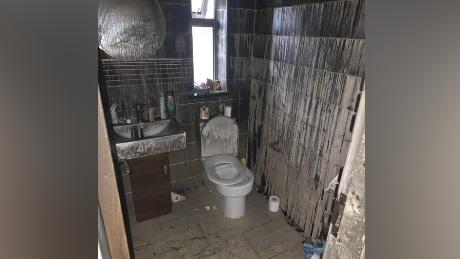 The bathroom with smoke and fire damage. The toilet is covered in soot as are the walls.