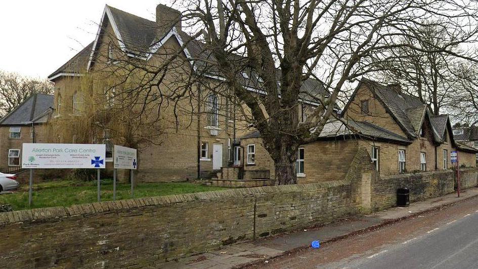 A large building set back from the roadside. There is a large tree at the front of the building and a sign outside which reads 'Allerton Park Care Centre'. 