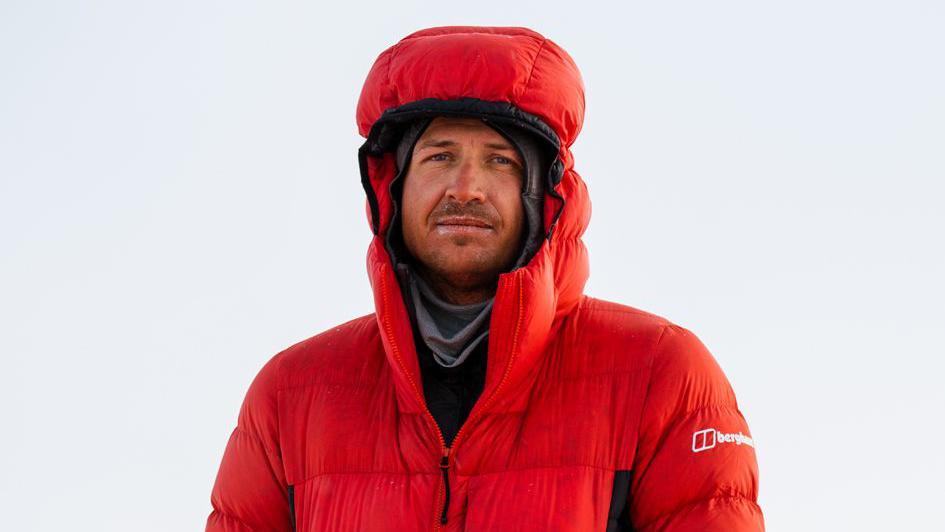 Former Rugby player and explorer Ed Jackson stands in Nepal wearing a red snowproof puffa jacket. 