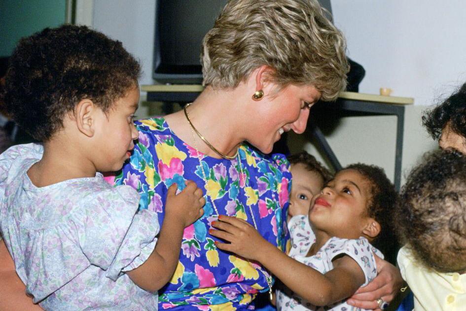 Princess Diana in a colourful patterned dress holds two small children in her arms. 