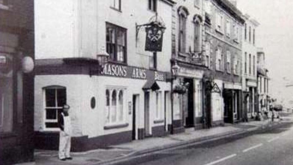 Black and white photograph of the Mason Arms building-with a blurry figure of a man standing next to it.