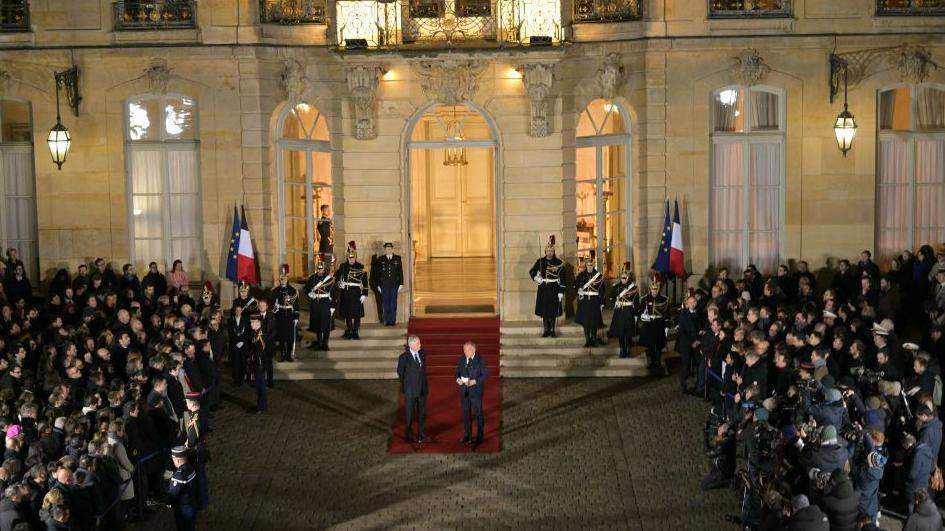 An audience outside the French prime minister's residence welcomes the new prime minister and says goodbye to his predecessor