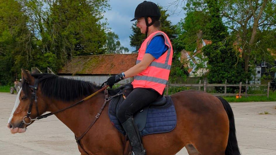 Amy in a high visibility vest and sat on a brown horse