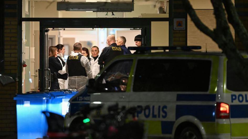 Police pictured inside Risbergska adult education centre at night, with a police van parked outside.