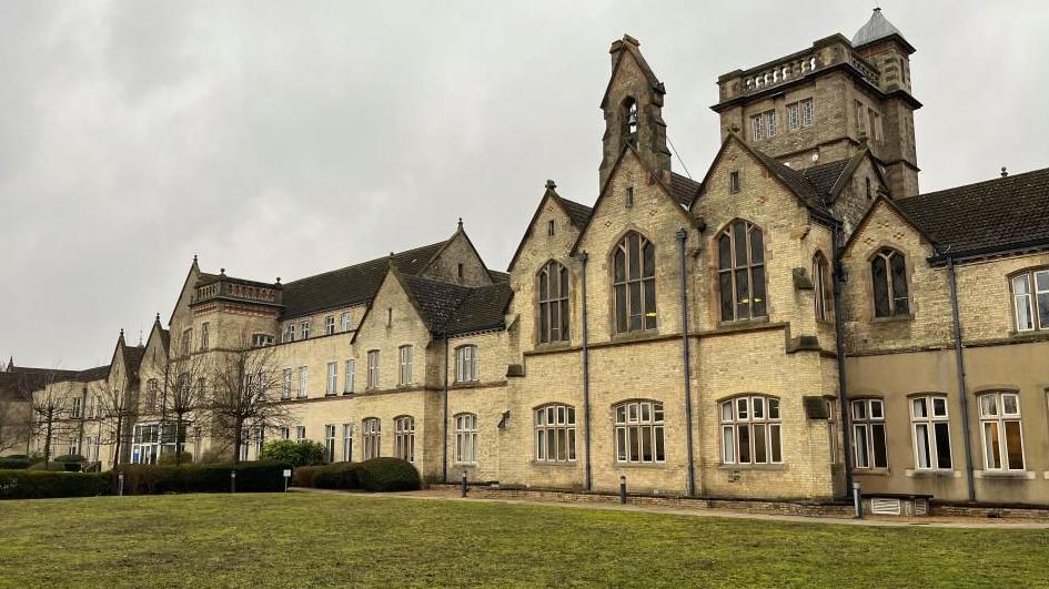 A large brick-built Victorian building. It has decorative windows and a lawn at the front