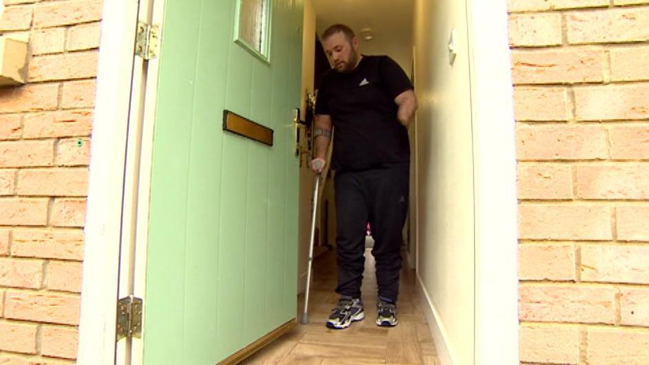 Jason Knight walking out of his front door, assisted by a crutch