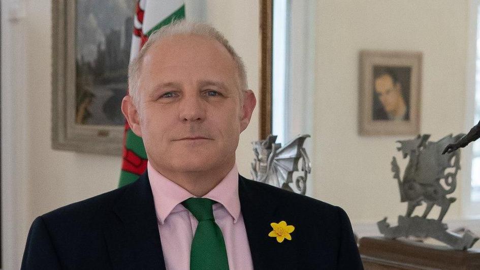 Veterans Commissioner Colonel James Phillips standing in front of a Welsh flag.