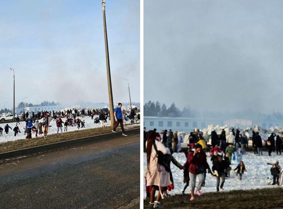 People stand in the snow and appear panicked. A large smoke cloud rises behind them.
