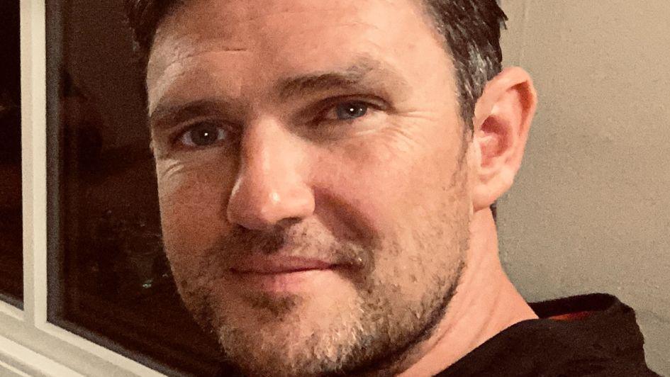 Dan Henshaw in a selfie. He has brown greying hair and a patchy beard. He is a white man. He looks to be in a living room or somewhere at home.