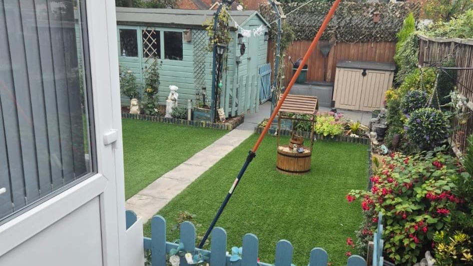 The home as it used to be with artificial lawns, a gate, painted shed, flowers and garden ornaments.