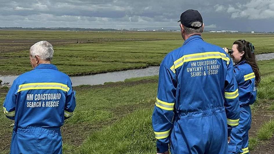 Three members of the HM Coastguard Search and Rescue crew look out towards the marshes