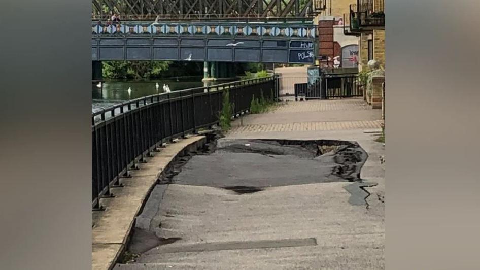 A sinkhole in the footpath along the River Nene with the town bridge in the distance.