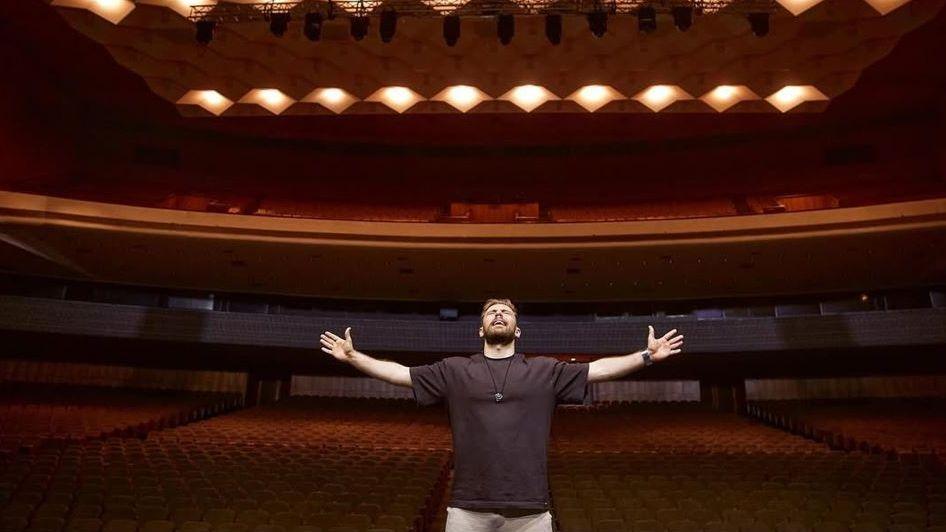 Anton Tymoshenko stands in the middle of a red theatre with his arms outstretched.