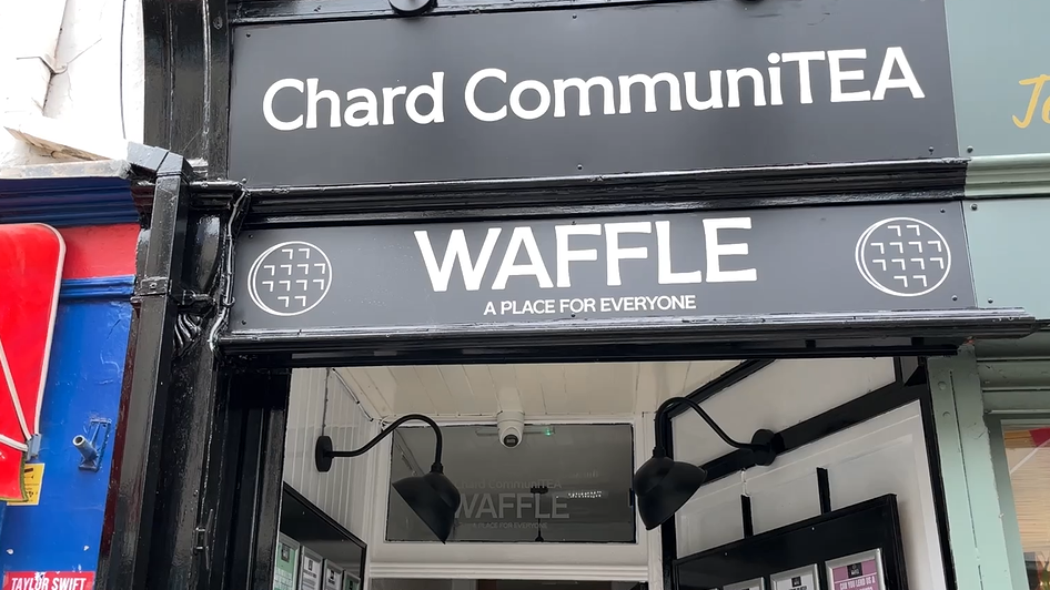 The entrance of the Chard CommuniTEA community cafe. The sign is black and white. It says Waffle and a place for everyone.