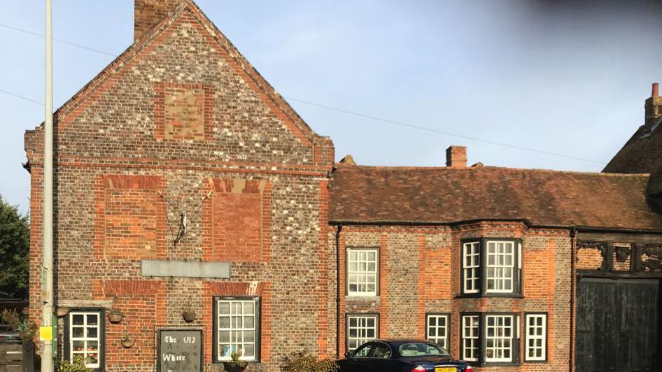 A large brick building that used to be a pub but is now a house and tea room. It has a tiled roof and the windows are black and white. There is a car parked outside.