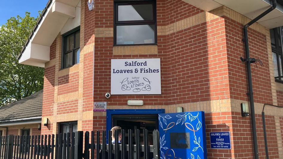 A sign for the charity Loaves and Fishes on a red brick building on a sunny day.