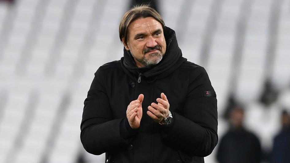 Daniel Farke, wearing a black coat and smiling, applauds at the end of Leeds' FA Cup quarter-final 