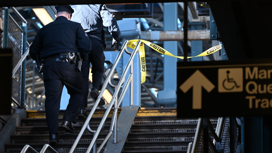 Police investigate at the Coney Island-Stillwell Avenue Station in Brooklyn after a woman aboard a subway car was set on fire and died. A police officer can be seen walking up a stair case with some yellow police tape flickering in the distance