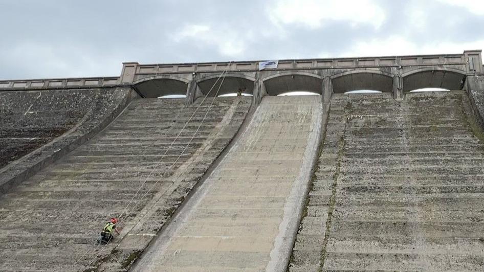 Man clearing a wall of the front of a reservoir using metal tools