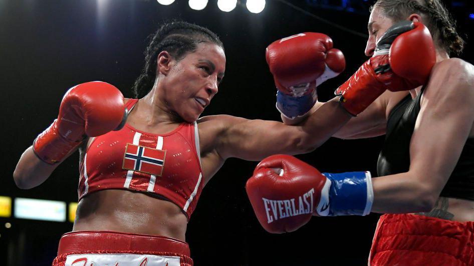 Cecilia Braekhus punches her opponent, wearing the Norway flag on her fight top