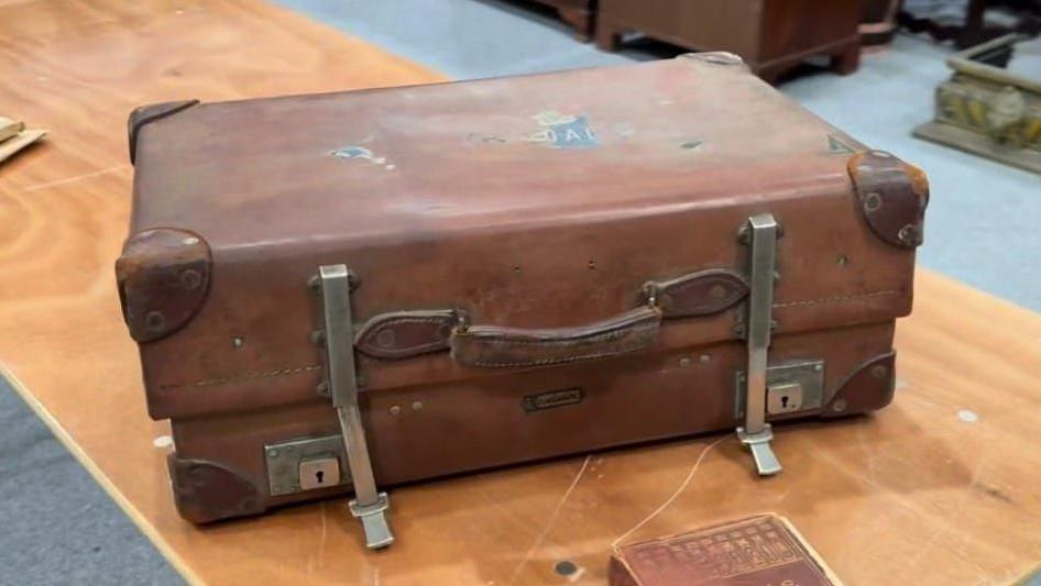 A brown leather suitcase with faded stickers on it.