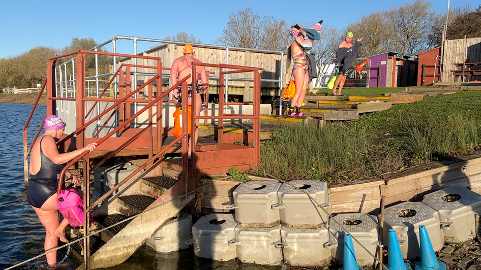 Four people getting in or out of the lake, with people drying themselves off or climbing out of it.