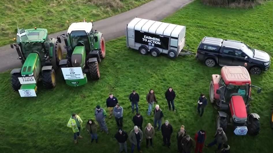 A group of about 20 people pictured from the air stand in front of a number of agricultural vehicles.