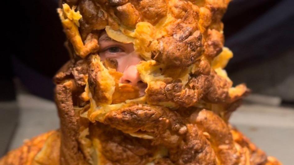 A boy covered in yorkshire puddings. Only his right eye and nose are visible underneath the crusty gooey goodness.