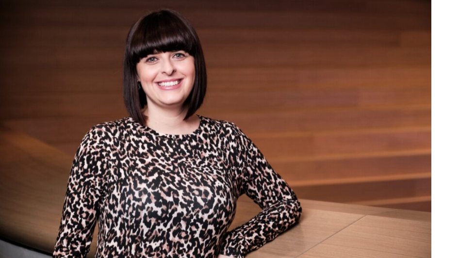 Rebeca with short brown hair in leopard print top stood in front of wood panelled wall