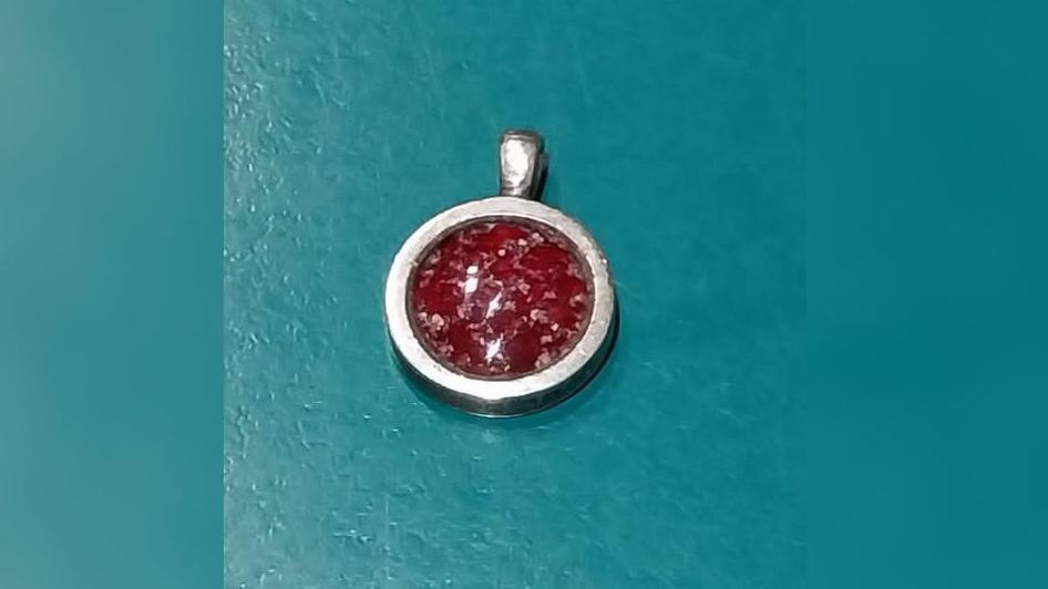 A silver round piece of jewellery with a red glass centre. The glass is flecked with what looks like silvery specks and the silver is slightly dented on the right side.