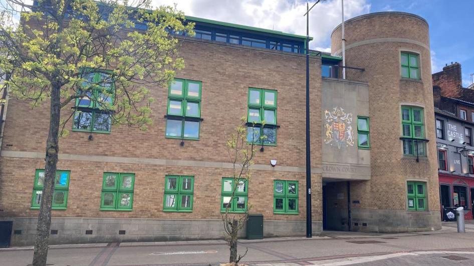 Luton Crown Court: A brown-brick building with numerous green-framed windows. A sign above the entrance says "CROWN COURT"