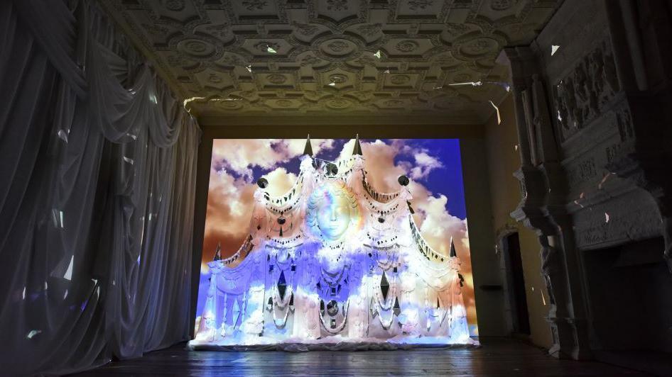 A huge wall carving at the end of a long high ceilinged hall is lit in shades of blue light.