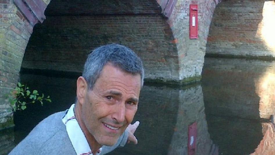 Uri Geller is pointing at a postbox on the side of a bridge, with a confused expression on his face