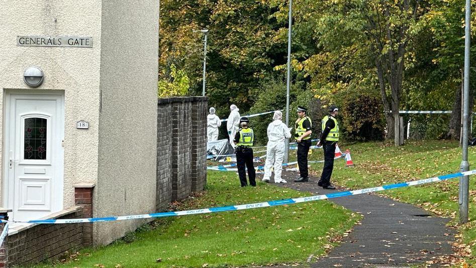 Uniformed police officers and forensic officers in white overalls standing outside a taped-off house on General's Gate
