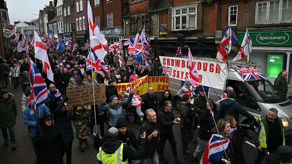 A large group of people protesting wave England flags and union jacks. Signs read "Crowborough says no"