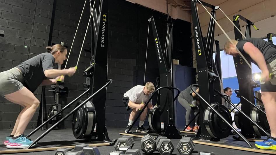 People in a gym working on SkiErg equipment with pulleys they are pulling down while bending their knees.