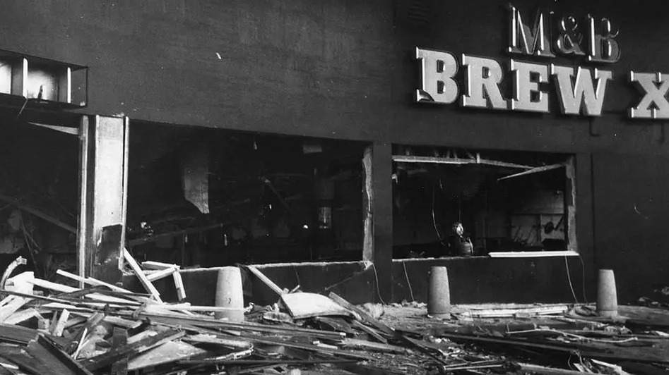 A black and white image of one of the pubs that was blown up in the city. Debris is on the floor with windows blown out below a M&B sign.