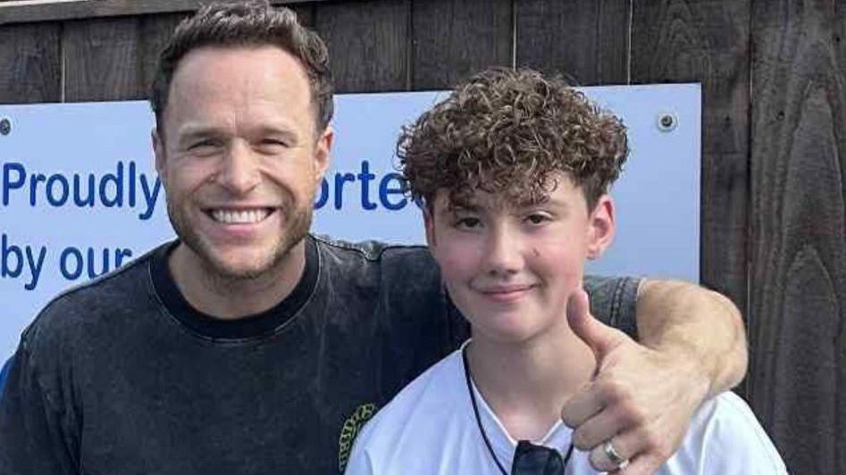 Olly Murs is smiling at the camera with his arm around young fan Charlie and doing a thumbs up.