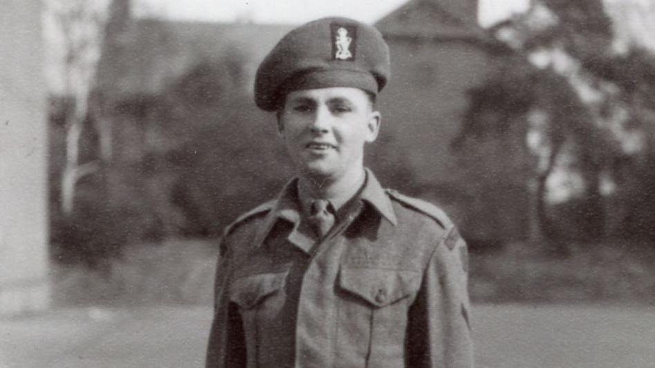 Black and white image showing Albert smiling, wearing uniform and Rifles cap, in front of trees