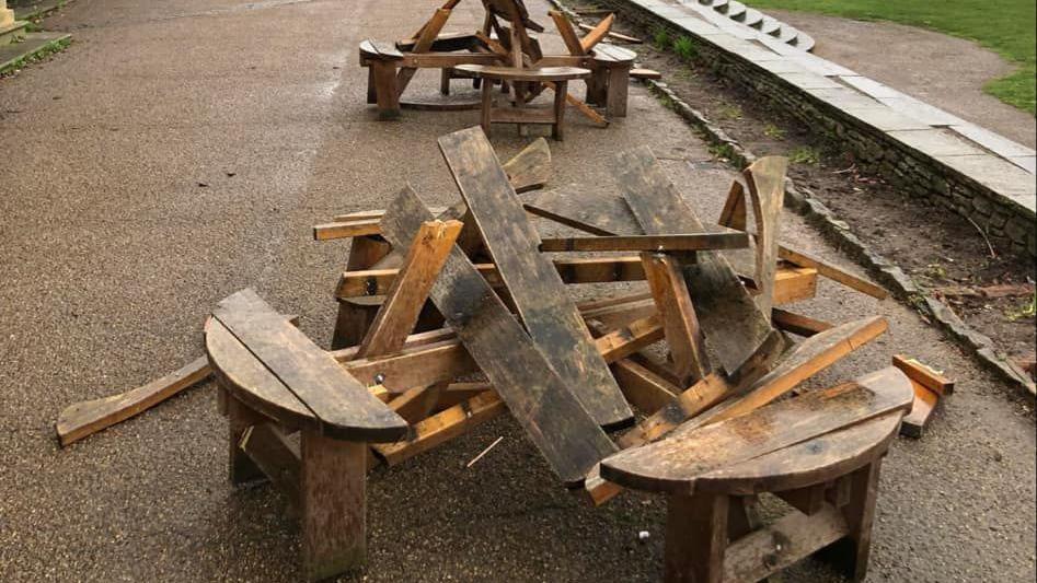 Two wooden benches in a row have been smashed up in a park. 