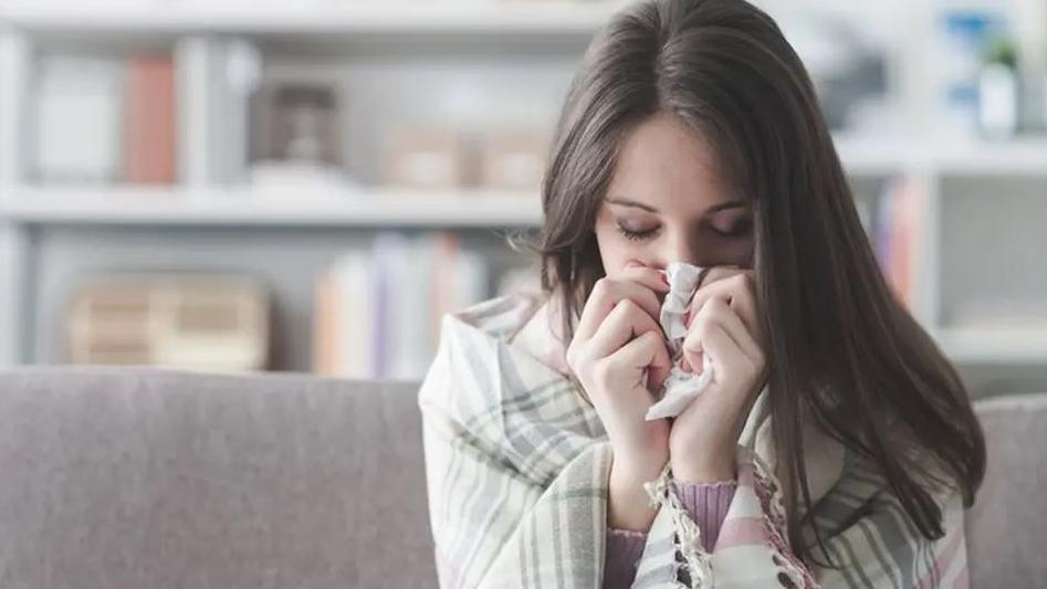 A woman blowing her nose while wrapped in a blanket.