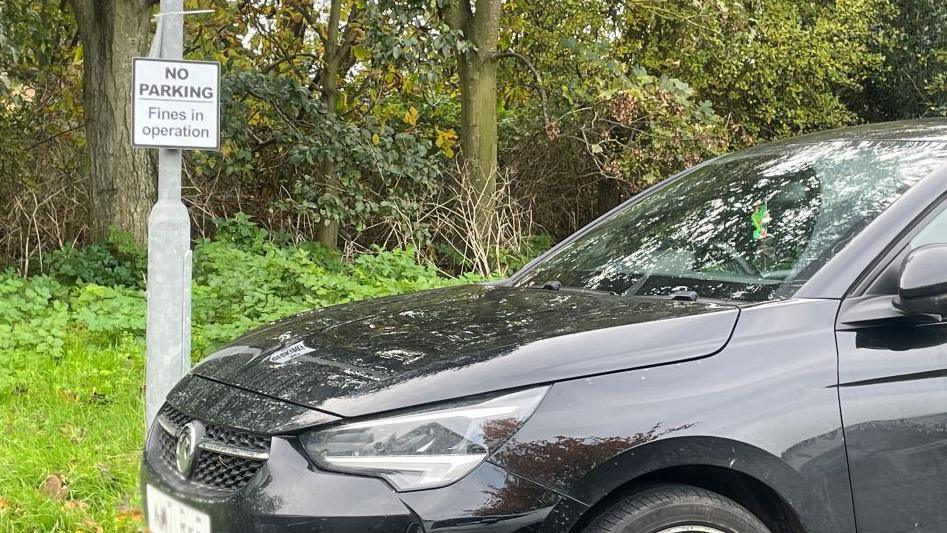 A car parked in front of a 'no parking' sign