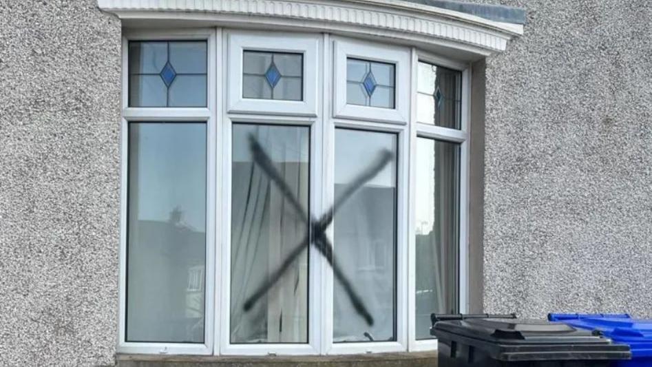 A black X sprayed across a white PVC bay window. 