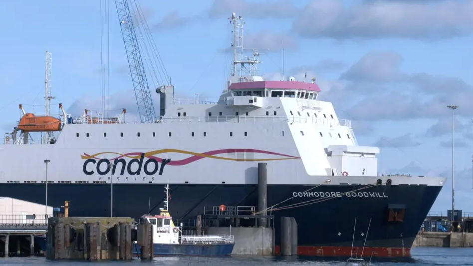 A large Condor shipping vessel, top half white and bottom half navy blue, with a large Condor Ferries sign on the side, docked at the harbour.