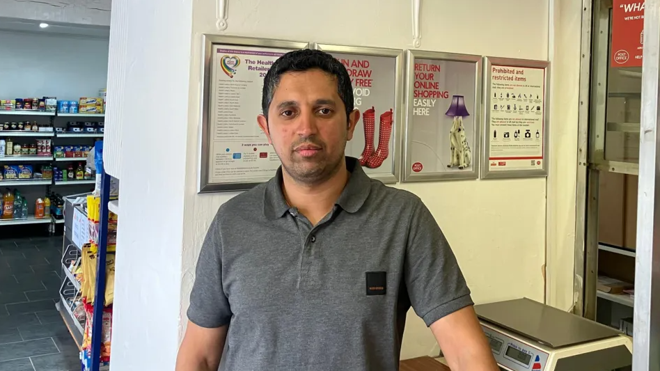 Arif wearing a grey T-shirt standing near the post office counter 