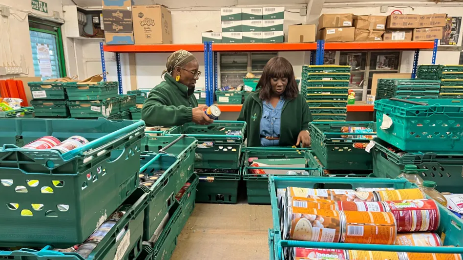 Two women sorting through green crates containing food in a food bank