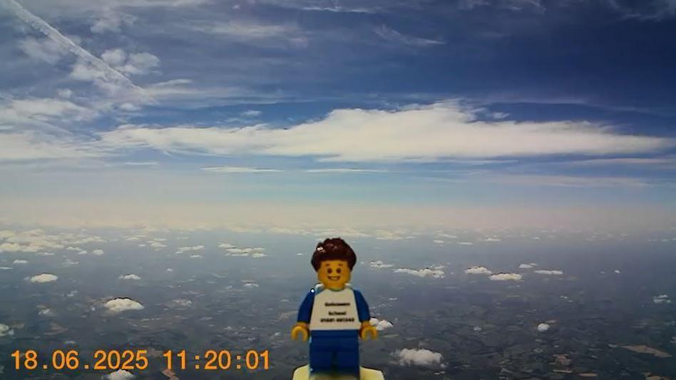 Dan the Lego man on his way above the clouds, with the countryside and houses visible below.