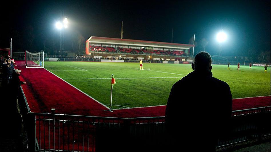 A silhouette of a person by the corner flag watching a game at Worthing's home ground.