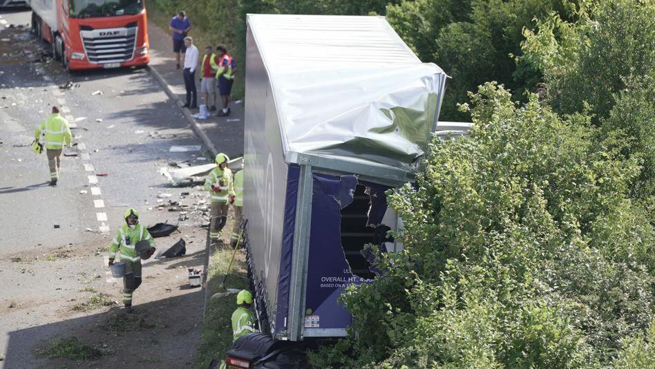A blue lorry trailer around which members of the emergency services are working.The vehicle has been in a crash and is surrounded by debris